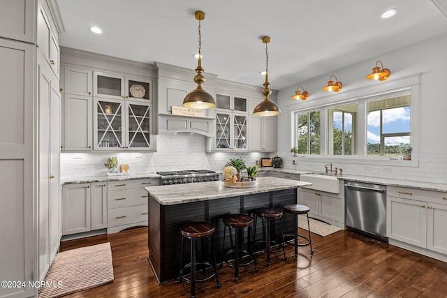 kitchen with decorative light fixtures, stainless steel appliances, light stone counters, a center island, and dark hardwood / wood-style floors