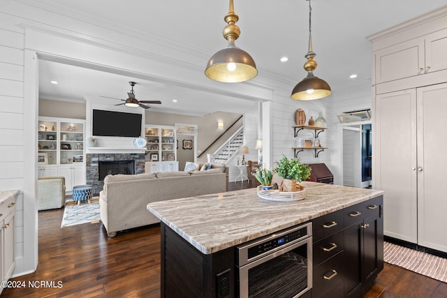 kitchen featuring dark wood-type flooring, ceiling fan, a kitchen island, and a stone fireplace