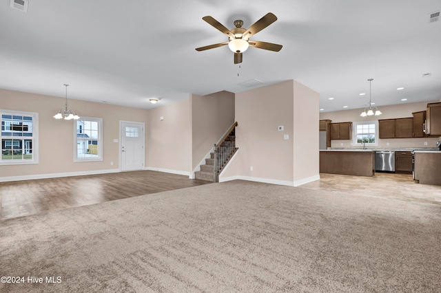 unfurnished living room featuring light wood-type flooring, a wealth of natural light, sink, and ceiling fan with notable chandelier