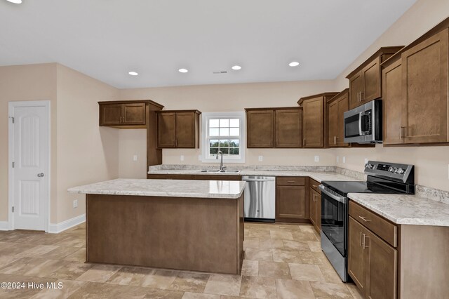 kitchen featuring appliances with stainless steel finishes, light stone counters, sink, and a center island