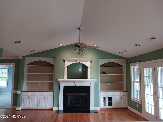 unfurnished living room featuring light wood-type flooring, vaulted ceiling, built in shelves, and ceiling fan