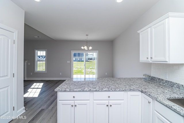 kitchen with light stone countertops, white cabinets, decorative backsplash, a chandelier, and dark hardwood / wood-style floors