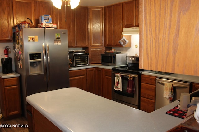 kitchen with a toaster, brown cabinetry, stainless steel appliances, light countertops, and under cabinet range hood