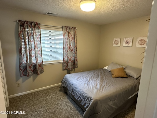 bedroom with a textured ceiling, dark colored carpet, visible vents, and baseboards