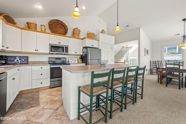 kitchen featuring visible vents, a center island, hanging light fixtures, vaulted ceiling, and stainless steel appliances