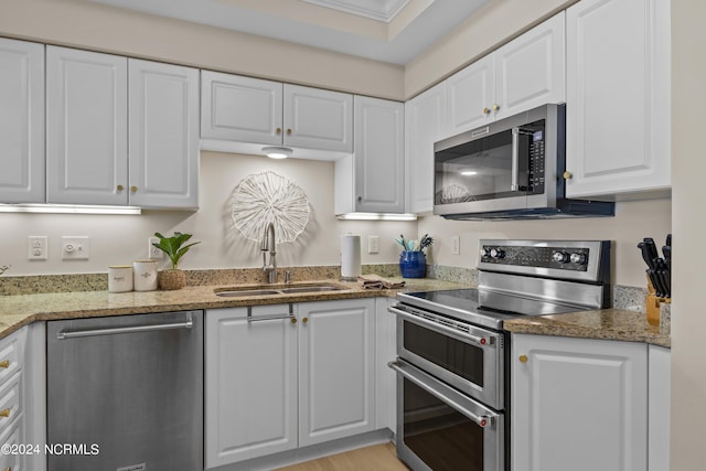 kitchen with light stone counters, white cabinetry, stainless steel appliances, and a sink