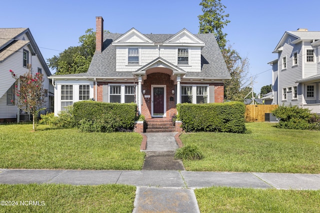 view of front of property featuring a shingled roof, a front yard, brick siding, and fence