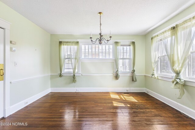 unfurnished dining area featuring a wealth of natural light, a textured ceiling, dark hardwood / wood-style flooring, and a chandelier