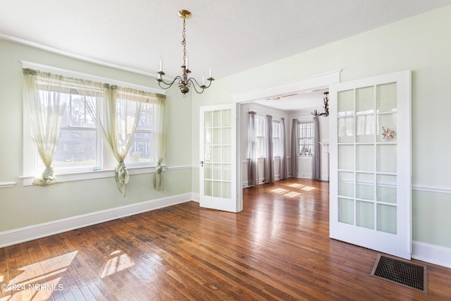 unfurnished room with a textured ceiling, a notable chandelier, french doors, and dark hardwood / wood-style floors