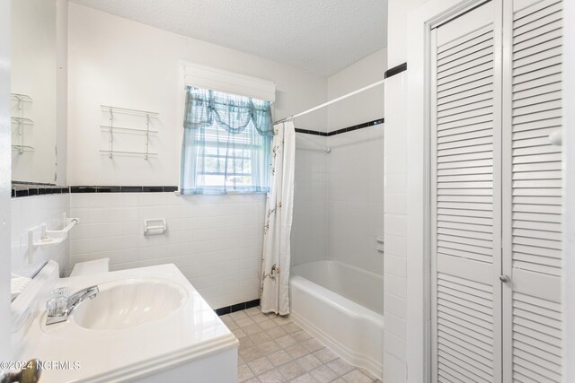 bathroom featuring vanity, shower / bathtub combination with curtain, tile patterned floors, a textured ceiling, and tile walls