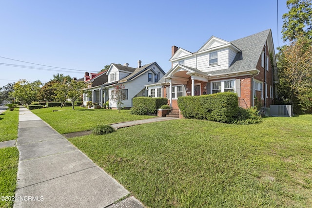 view of front facade with a front yard, central air condition unit, brick siding, and roof with shingles