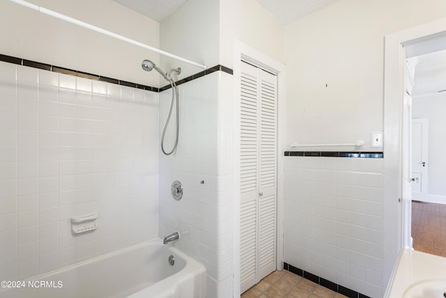 full bath with a wainscoted wall, tile walls, a closet, bathtub / shower combination, and a textured ceiling