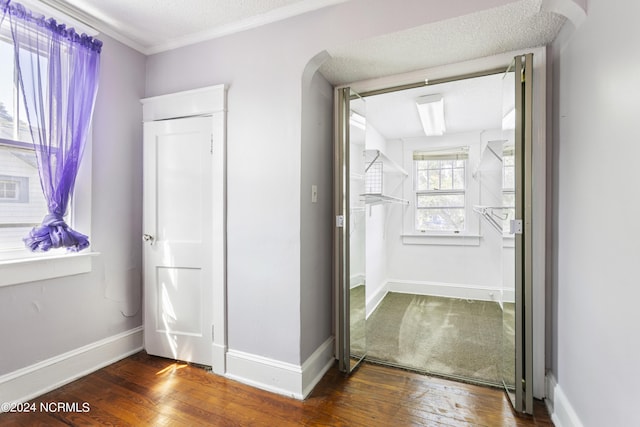 corridor with hardwood / wood-style flooring, baseboards, a textured ceiling, and ornamental molding