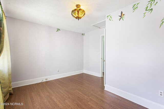 unfurnished room with attic access, a textured ceiling, baseboards, and wood finished floors