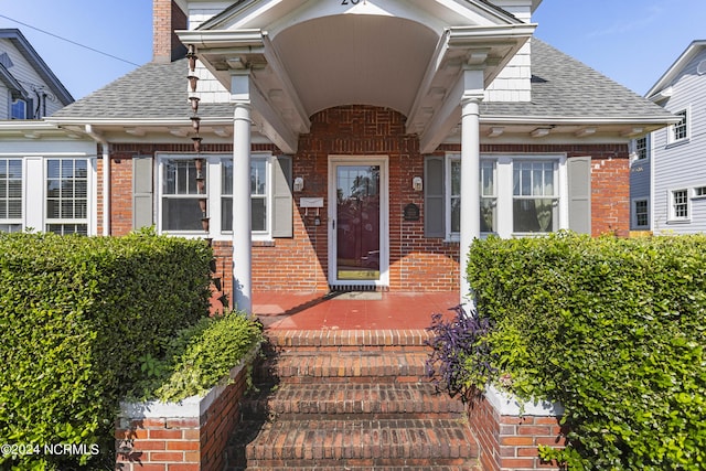 view of exterior entry featuring a shingled roof, brick siding, and a chimney