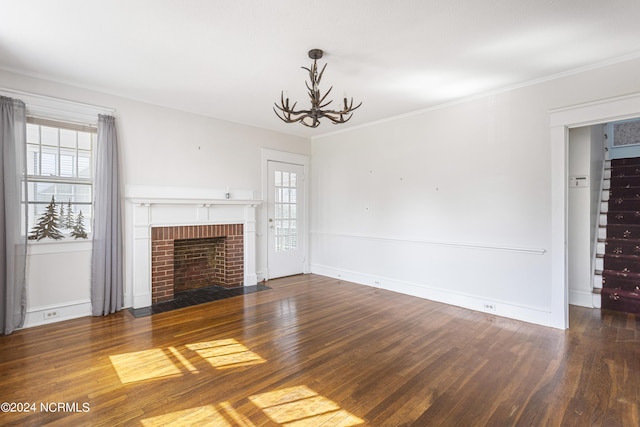 unfurnished living room featuring crown molding, a brick fireplace, a notable chandelier, and hardwood / wood-style flooring