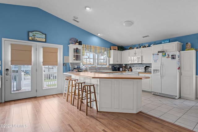 kitchen with white appliances, a kitchen breakfast bar, vaulted ceiling, white cabinets, and glass insert cabinets