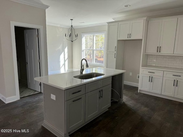 kitchen featuring pendant lighting, sink, white cabinetry, ornamental molding, and an island with sink