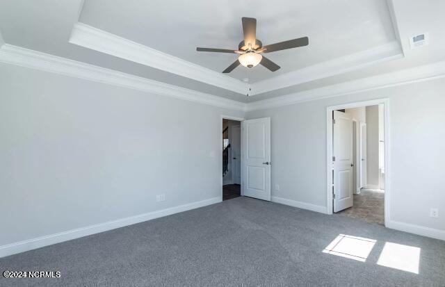 unfurnished bedroom with ceiling fan, a raised ceiling, carpet, and crown molding