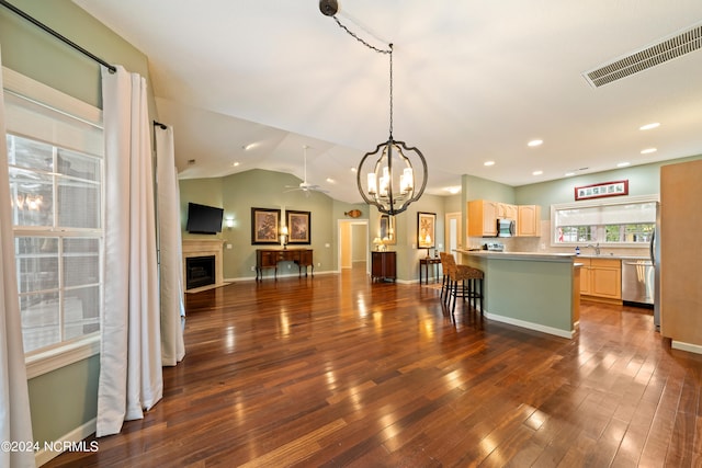 kitchen with vaulted ceiling, ceiling fan with notable chandelier, light brown cabinetry, dark hardwood / wood-style flooring, and stainless steel appliances