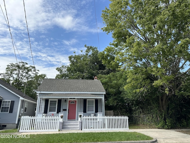 bungalow-style home featuring covered porch, a fenced front yard, a chimney, and roof with shingles