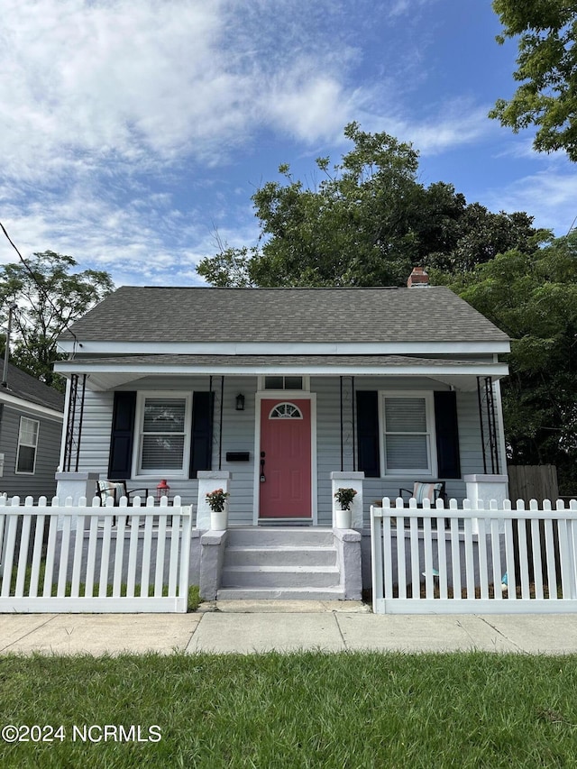 bungalow-style home with a fenced front yard, covered porch, and roof with shingles