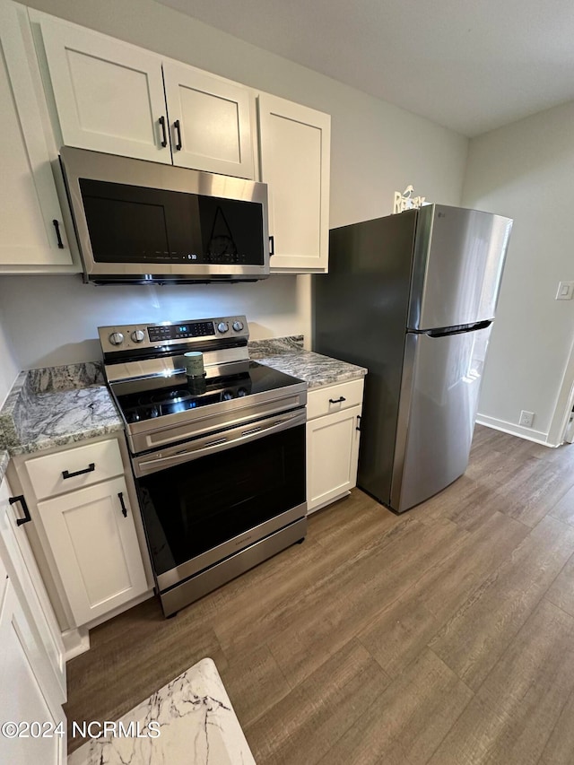 kitchen with appliances with stainless steel finishes, light stone countertops, white cabinetry, and dark hardwood / wood-style flooring