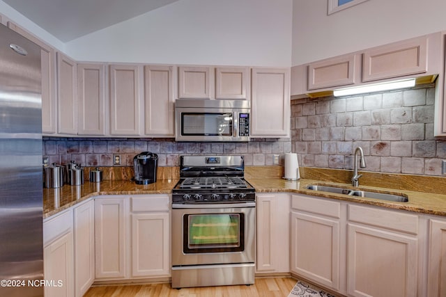 kitchen with light stone counters, decorative backsplash, appliances with stainless steel finishes, vaulted ceiling, and a sink