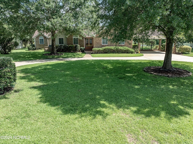 view of property hidden behind natural elements with a front yard, brick siding, and driveway