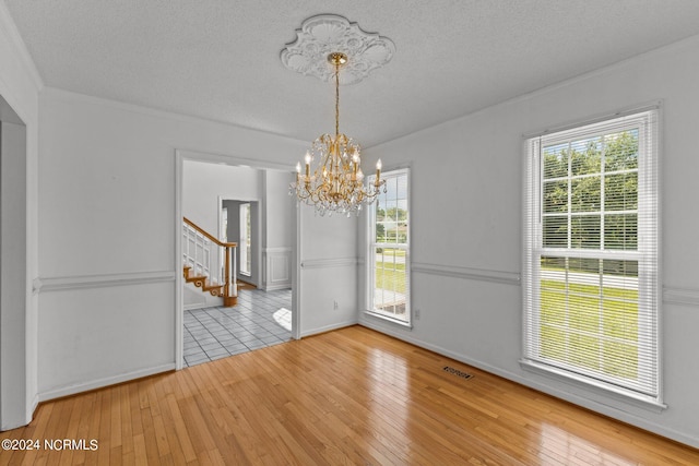 unfurnished dining area with light wood-type flooring, a textured ceiling, and a notable chandelier