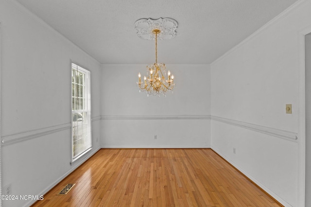 unfurnished dining area featuring a chandelier, light wood-style flooring, visible vents, baseboards, and crown molding