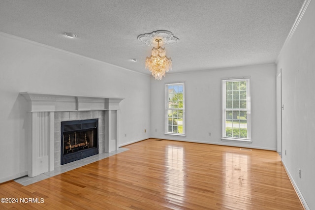 unfurnished living room featuring an inviting chandelier, a tile fireplace, light wood-type flooring, a textured ceiling, and crown molding