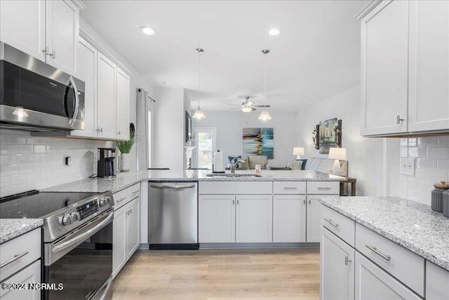 kitchen with a peninsula, a sink, open floor plan, appliances with stainless steel finishes, and light wood finished floors