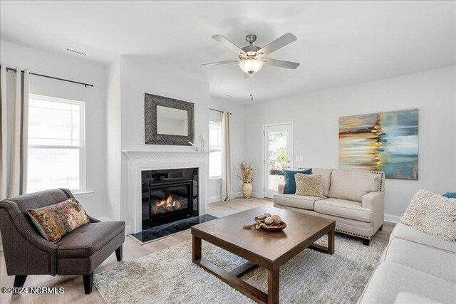 living area with light wood-type flooring, a glass covered fireplace, visible vents, and plenty of natural light