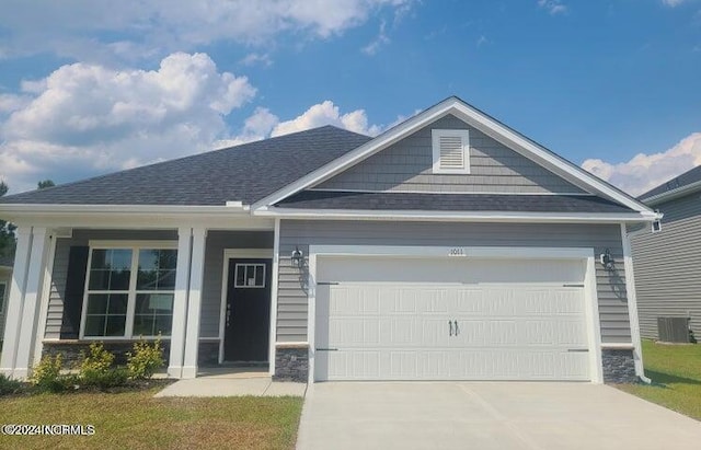 craftsman-style house with central AC unit, a garage, a shingled roof, driveway, and stone siding