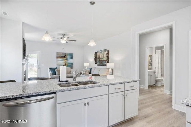 kitchen with a sink, open floor plan, hanging light fixtures, stainless steel dishwasher, and light stone countertops