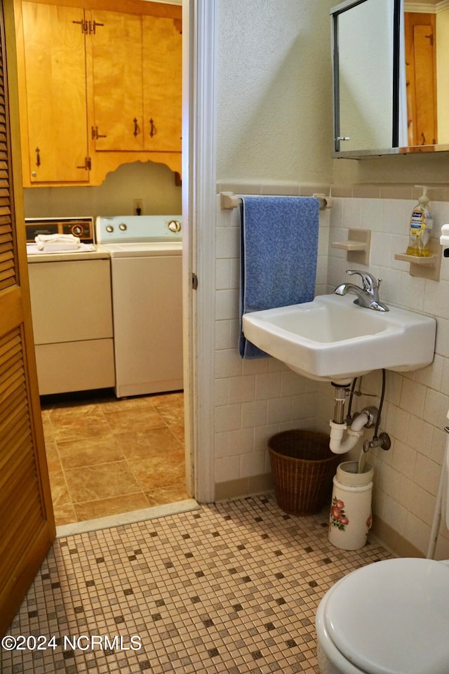 bathroom featuring washer and dryer, sink, toilet, tile patterned floors, and tile walls