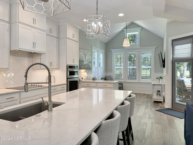 kitchen featuring pendant lighting, sink, stainless steel double oven, light wood-type flooring, and white cabinets