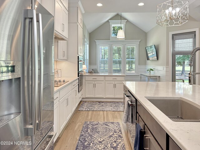 kitchen with hanging light fixtures, light hardwood / wood-style flooring, light stone countertops, stainless steel appliances, and white cabinetry