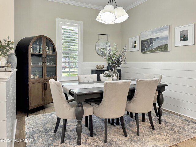 dining area featuring light wood-type flooring, wooden walls, a notable chandelier, and ornamental molding