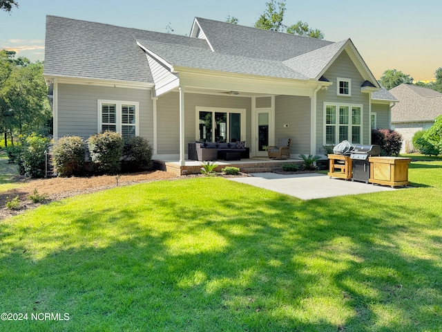 back house at dusk with a yard, ceiling fan, a patio, and outdoor lounge area