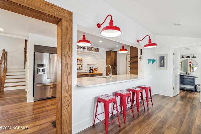 kitchen with high end refrigerator, a kitchen breakfast bar, a peninsula, light countertops, and pendant lighting