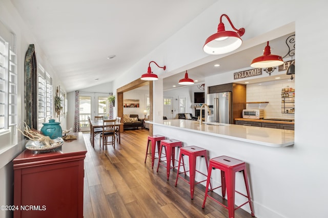 kitchen with high end refrigerator, dark wood finished floors, vaulted ceiling, light countertops, and a kitchen bar