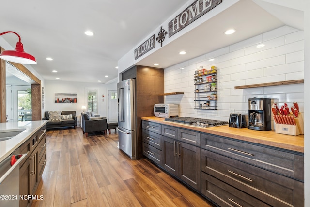 kitchen featuring dark brown cabinetry, stainless steel appliances, dark wood-type flooring, wooden counters, and decorative backsplash