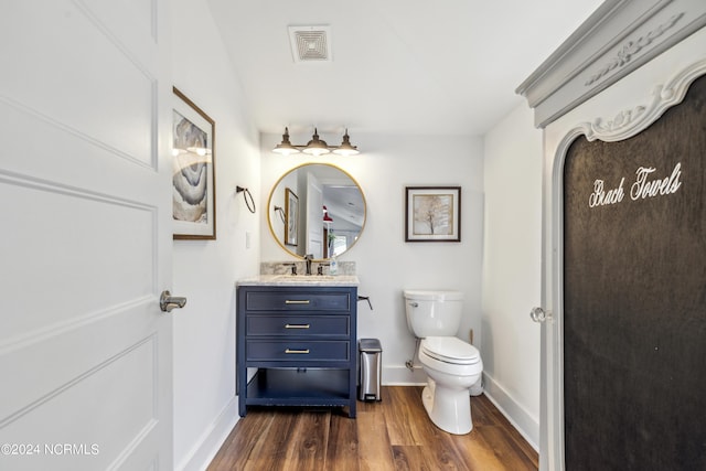 half bathroom with toilet, wood finished floors, vanity, visible vents, and baseboards