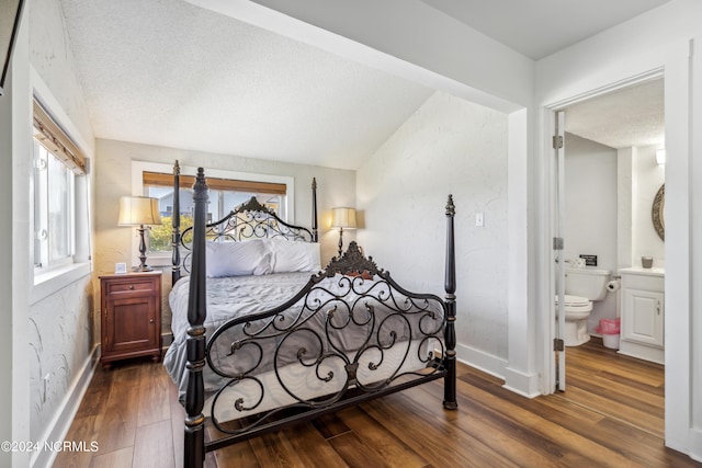 bedroom with a textured ceiling, dark wood-style flooring, baseboards, vaulted ceiling, and ensuite bath