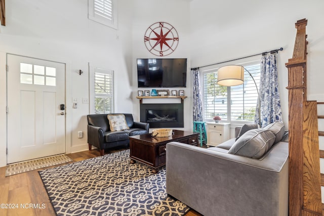 living area with a glass covered fireplace, wood finished floors, and a towering ceiling