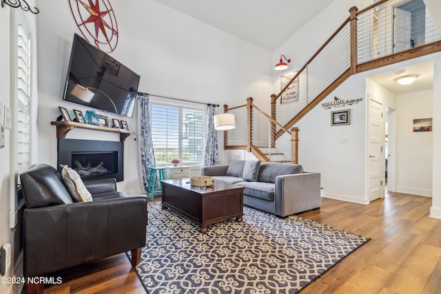 living room featuring a high ceiling, stairway, a fireplace, and wood finished floors