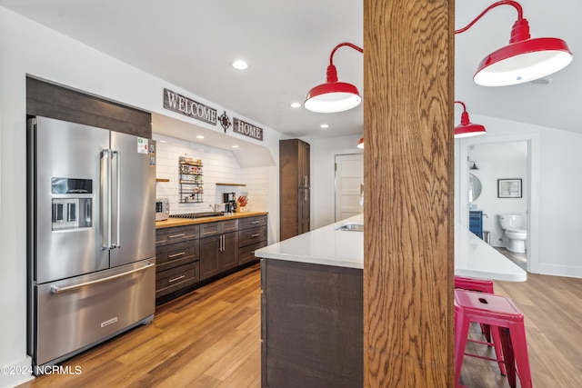 kitchen featuring dark brown cabinetry, a kitchen breakfast bar, high end fridge, light countertops, and tasteful backsplash