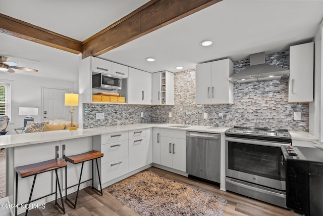 kitchen with appliances with stainless steel finishes, decorative backsplash, white cabinets, and wall chimney range hood